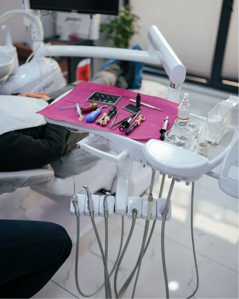 Dentist's office with tools on pink mat. A patient reclines in the chair. Bright, clean space with dental instruments and modern equipment.