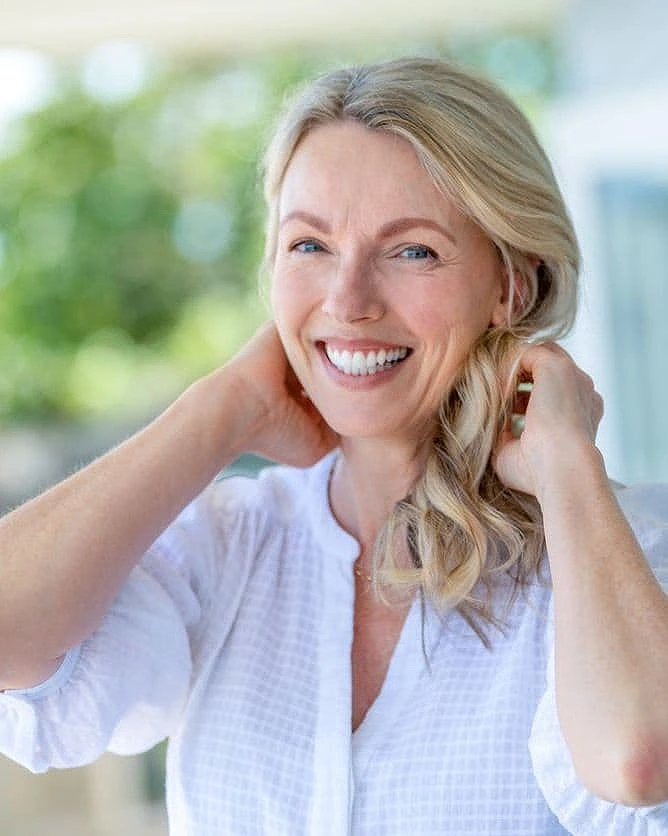 Smiling mature woman with healthy white teeth and blonde hair outdoors, showcasing a confident smile after cosmetic or restorative dental treatment.