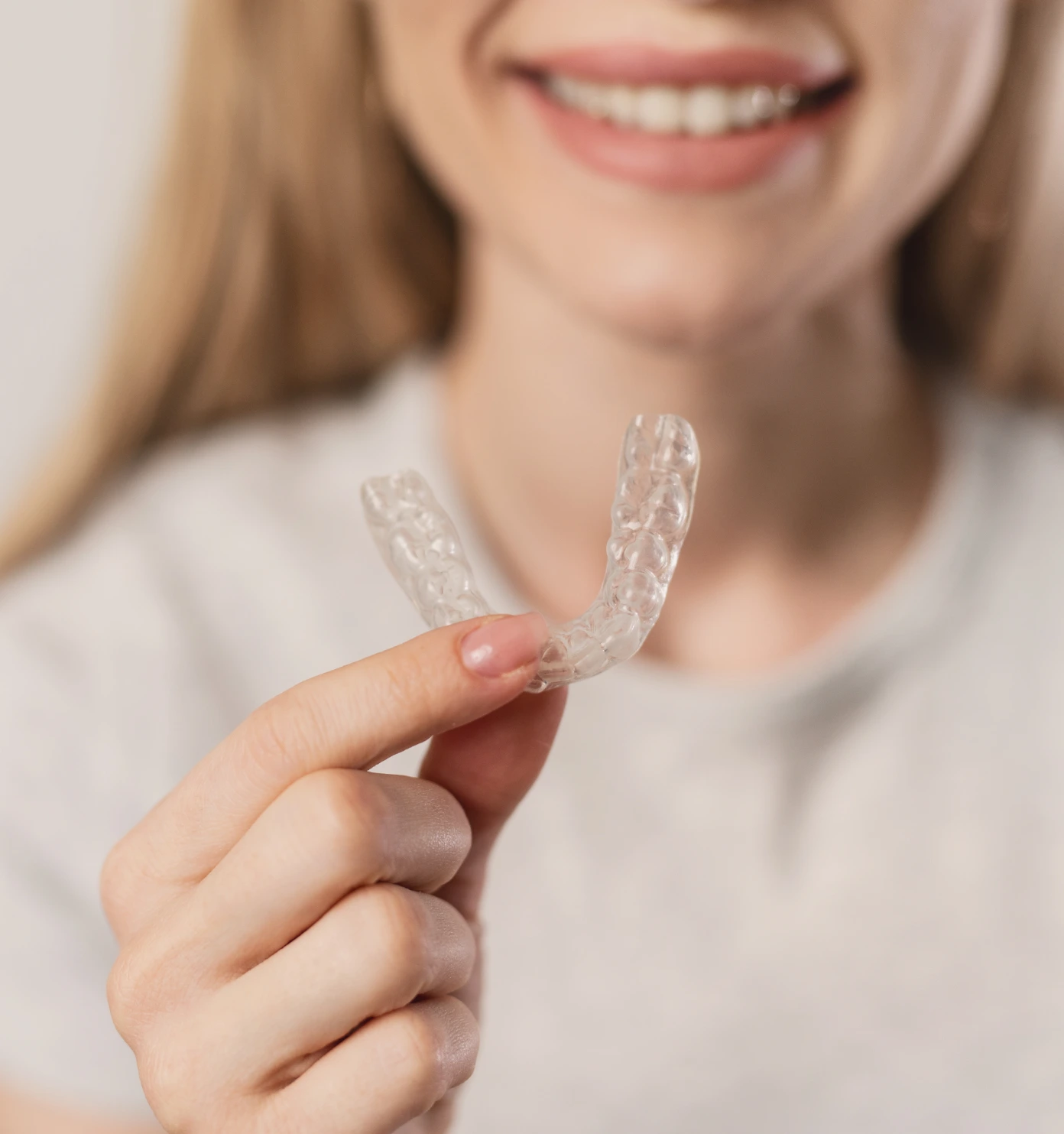 Person holding a clear dental aligner in front of a smiling mouth.